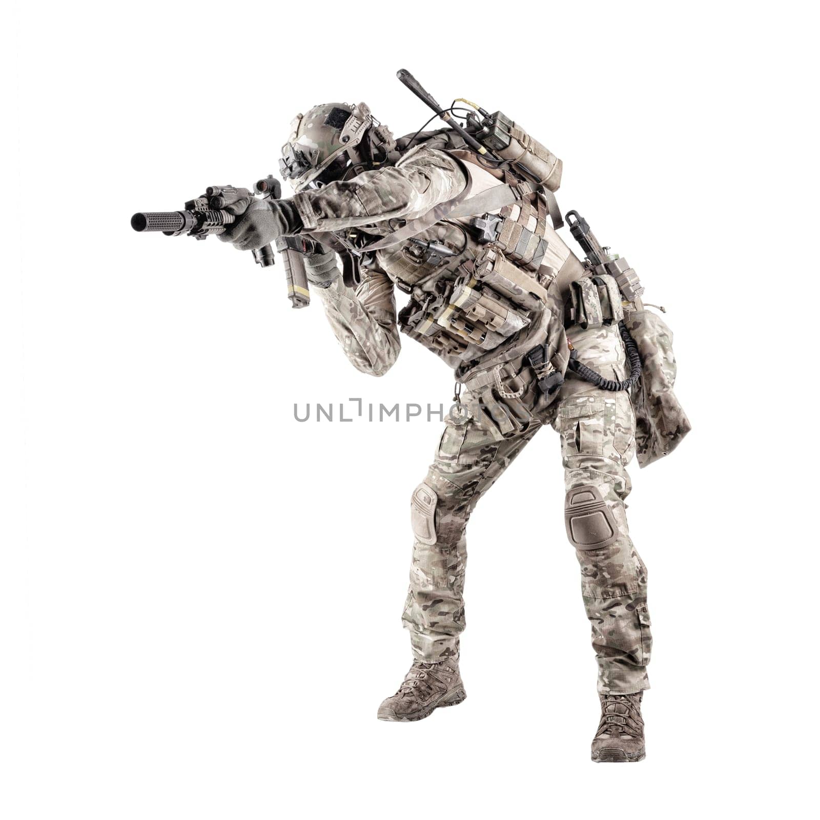 Modern army infantry rifleman in camo uniform, radio headset on helmet, ammo on load carrier, sneaking, crouching, aiming and shooting with service rifle studio shoot isolated on white background