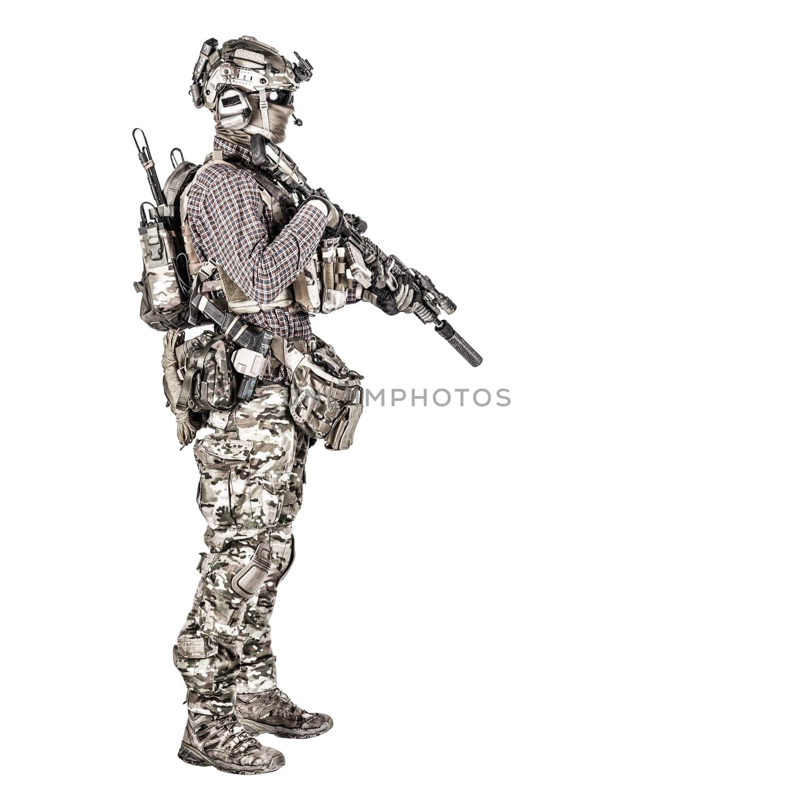 Full length portrait of airsoft player in checkered shirt, wearing camouflage uniform, helmet with tactical radio headset, body armour, aiming with service rifle replica studio shoot isolated on white