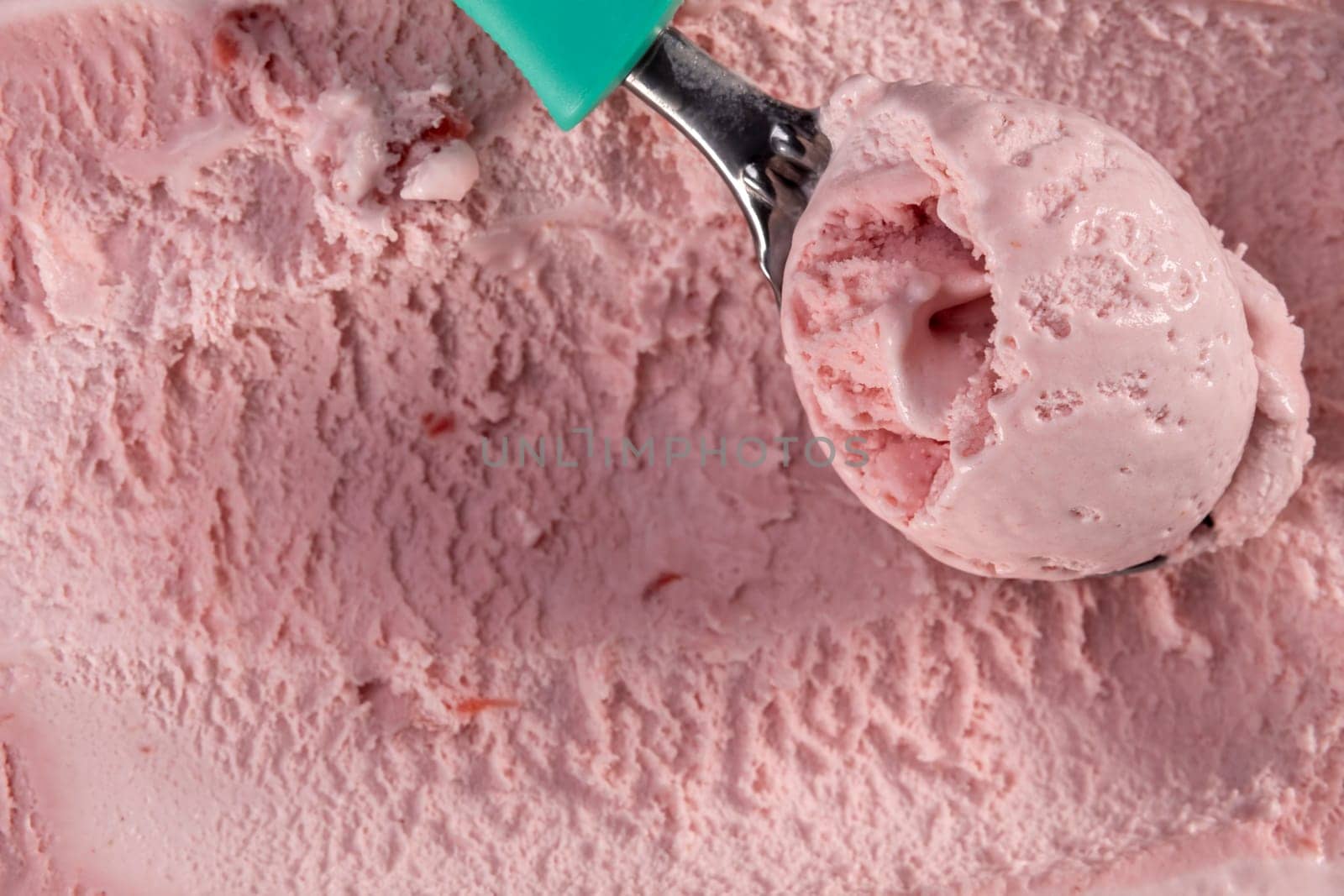 Top view of strawberry flavour ice cream with scoop in box. Focus on scoop with ice cream.