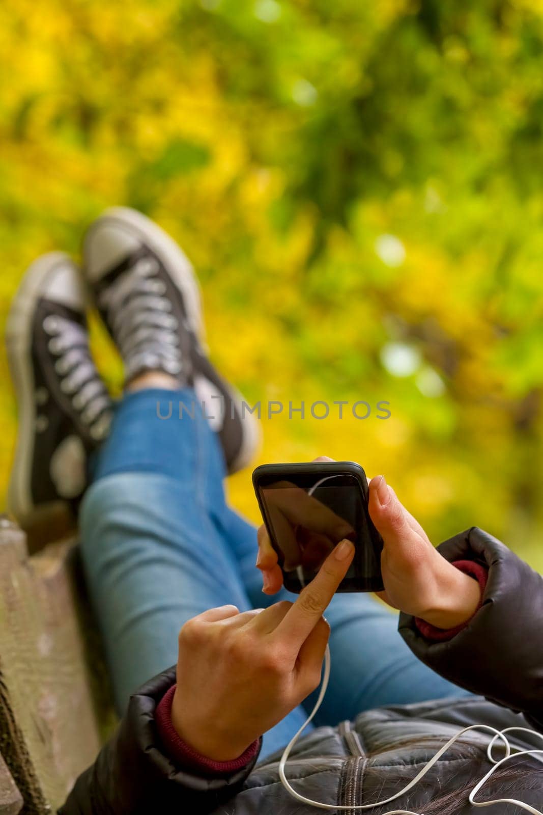 Teenage girl using smartphone lying on the bench in autumn park. Focus on smart phone.
