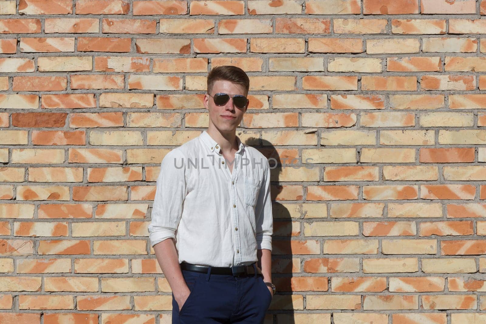 Smiling young man portrait with retro shiny drop sunglasses against brick wall