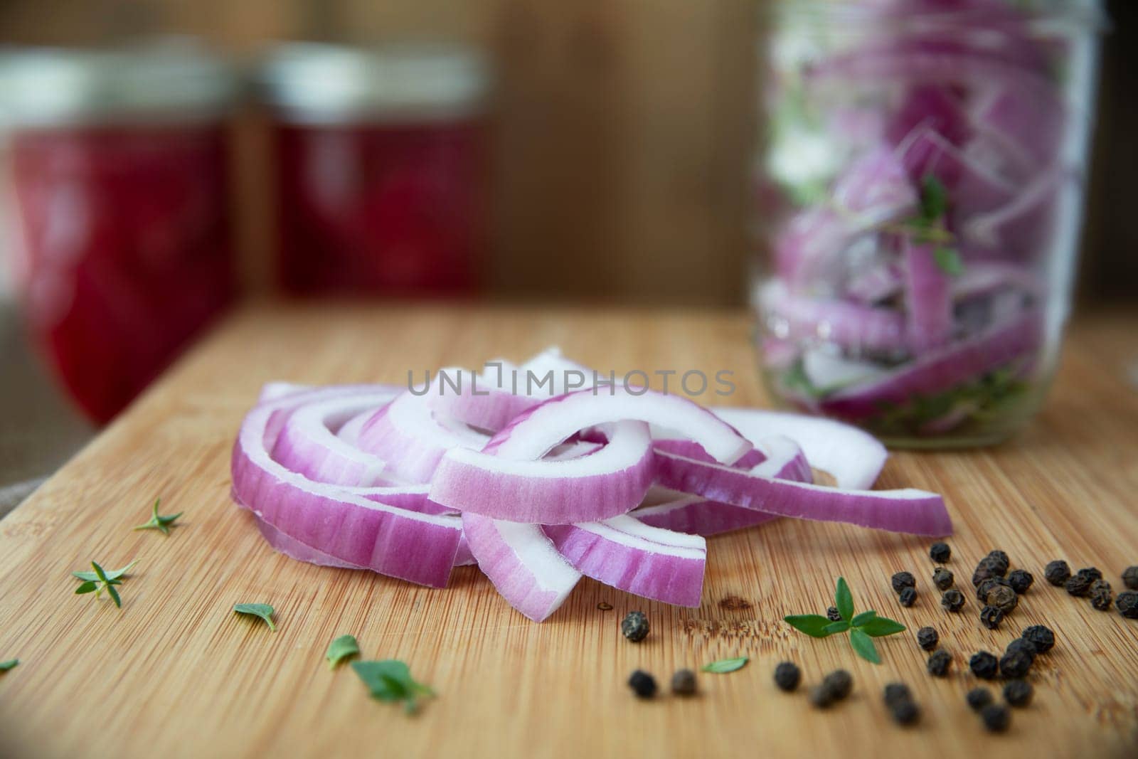 Red onion slices, thyme and peppercorns  on cutting board with jars for pickling.