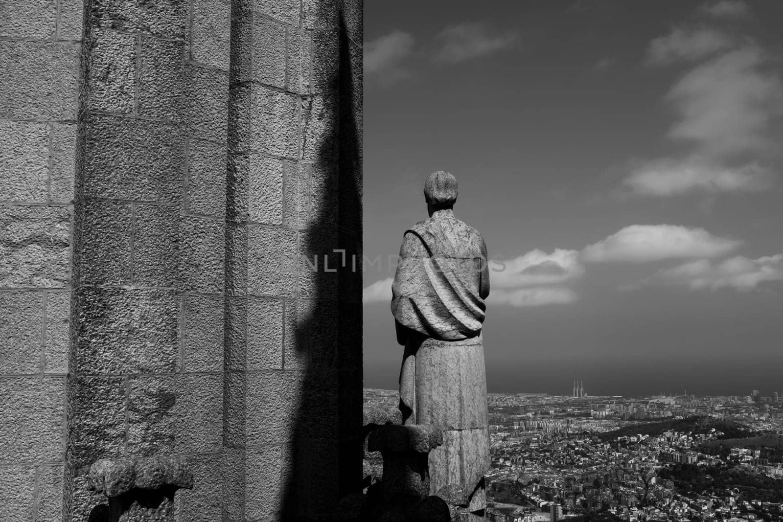 Statue of an Apostle crowing the roof of the Temple Expiatori del Sagrat Cor (Expiatory Church of the Sacred Heart) Beyond the sculpture, enjoyment a breathtaking view of the city of Barcelona.