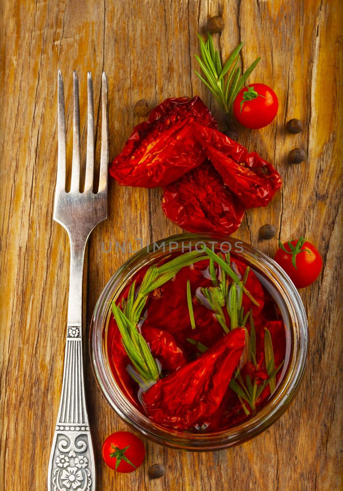 Delicious dried tomatoes in the jar of olive oil, the fork on wood background. In rustic style.