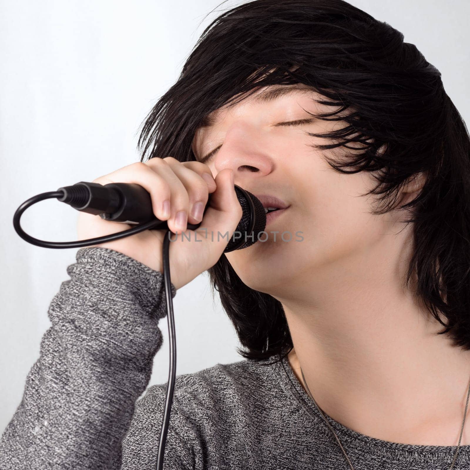 Black hair young guy in emo style is singing in microphone on white background.