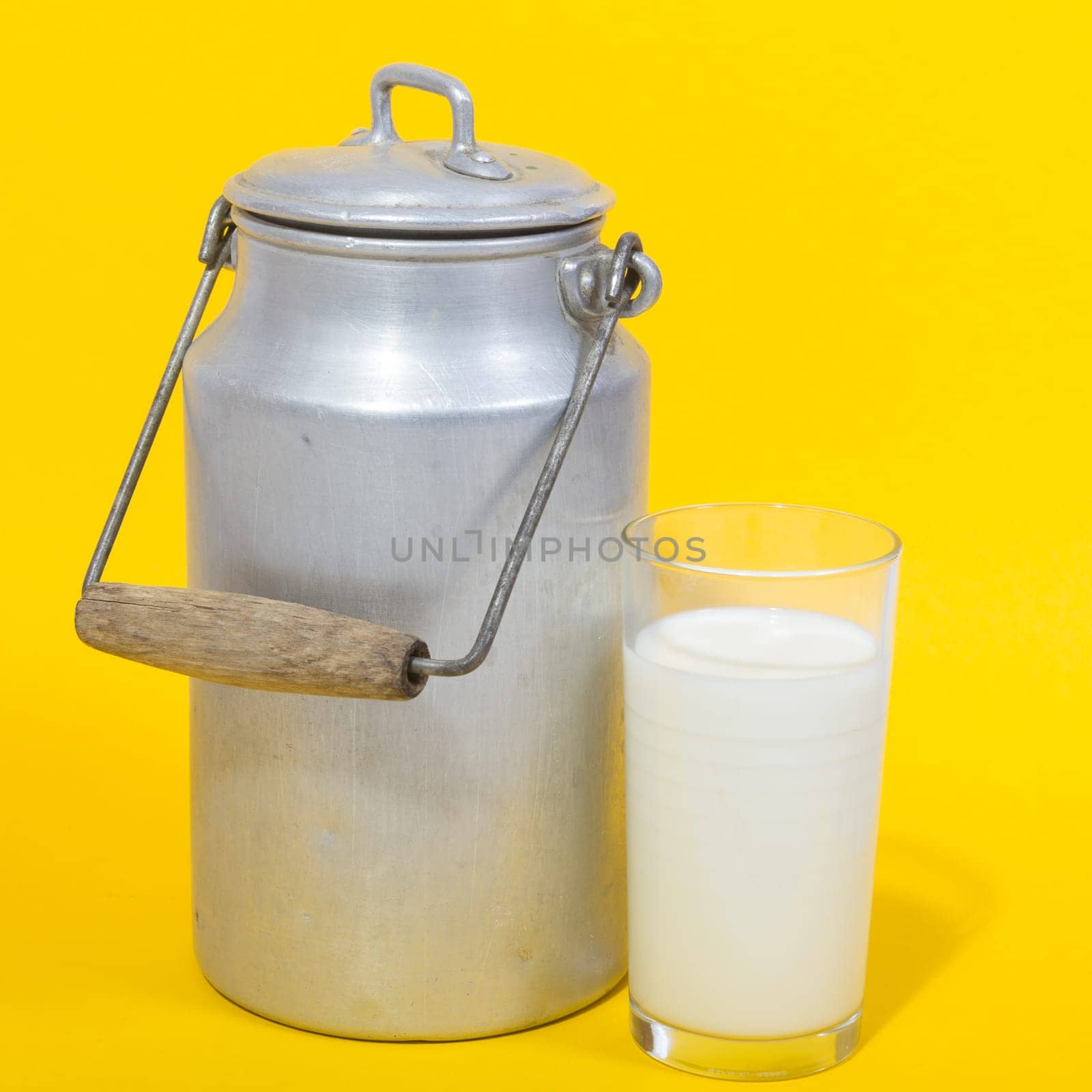 Glass of fresh milk and retro milk canister on yellow background