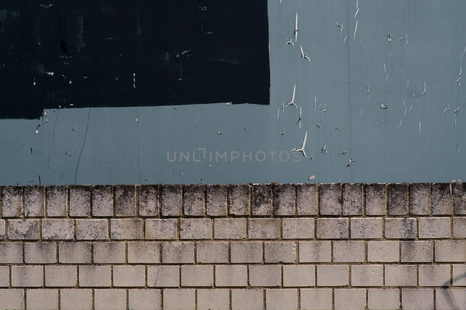 The close-up of a gray billboard with torn pieces of paper over a bright wall edge...