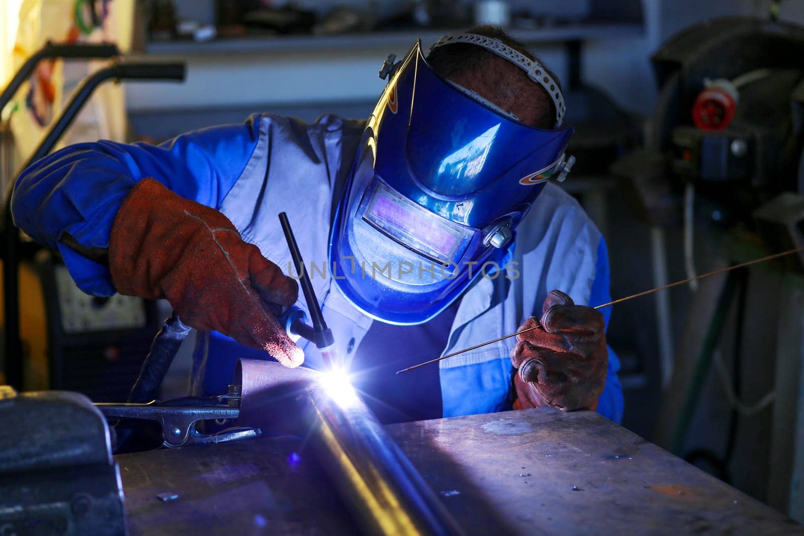A worker welds a pipe with inert gas in a workshop.
