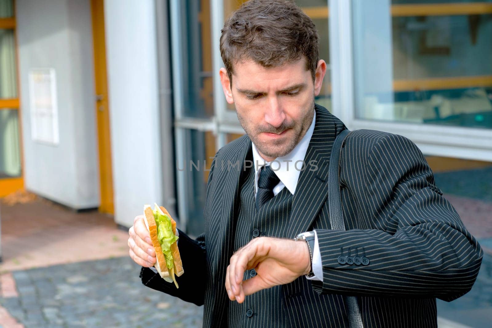 businessman in suit in front of city- background is eating and looking for time