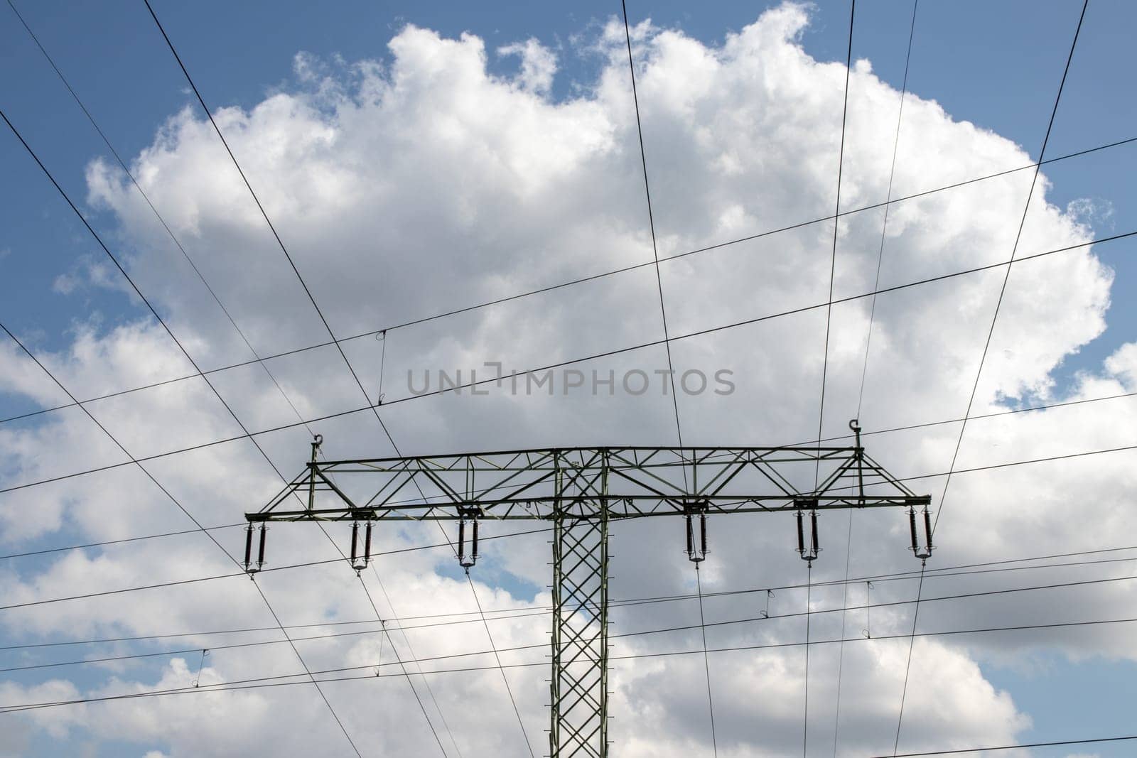 Power generation, transmission and distribution concept. Close-up of a electricity supply pylon and the high voltage power lines against a blue cloudy sky. Facilities for the transmission of electrical energy.