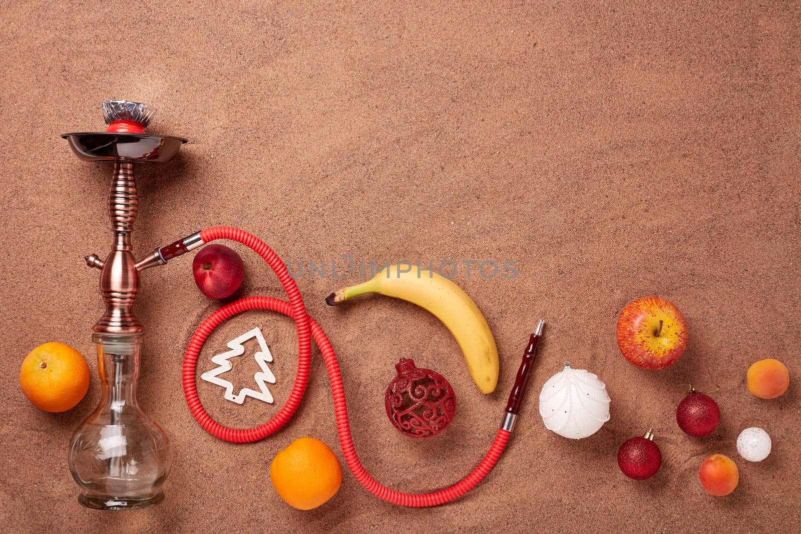 Hookah (shisha), fruit and christmas ornaments on sand background. Top view. New Year and Christmas. Winter vacation in warm countries, beach holiday