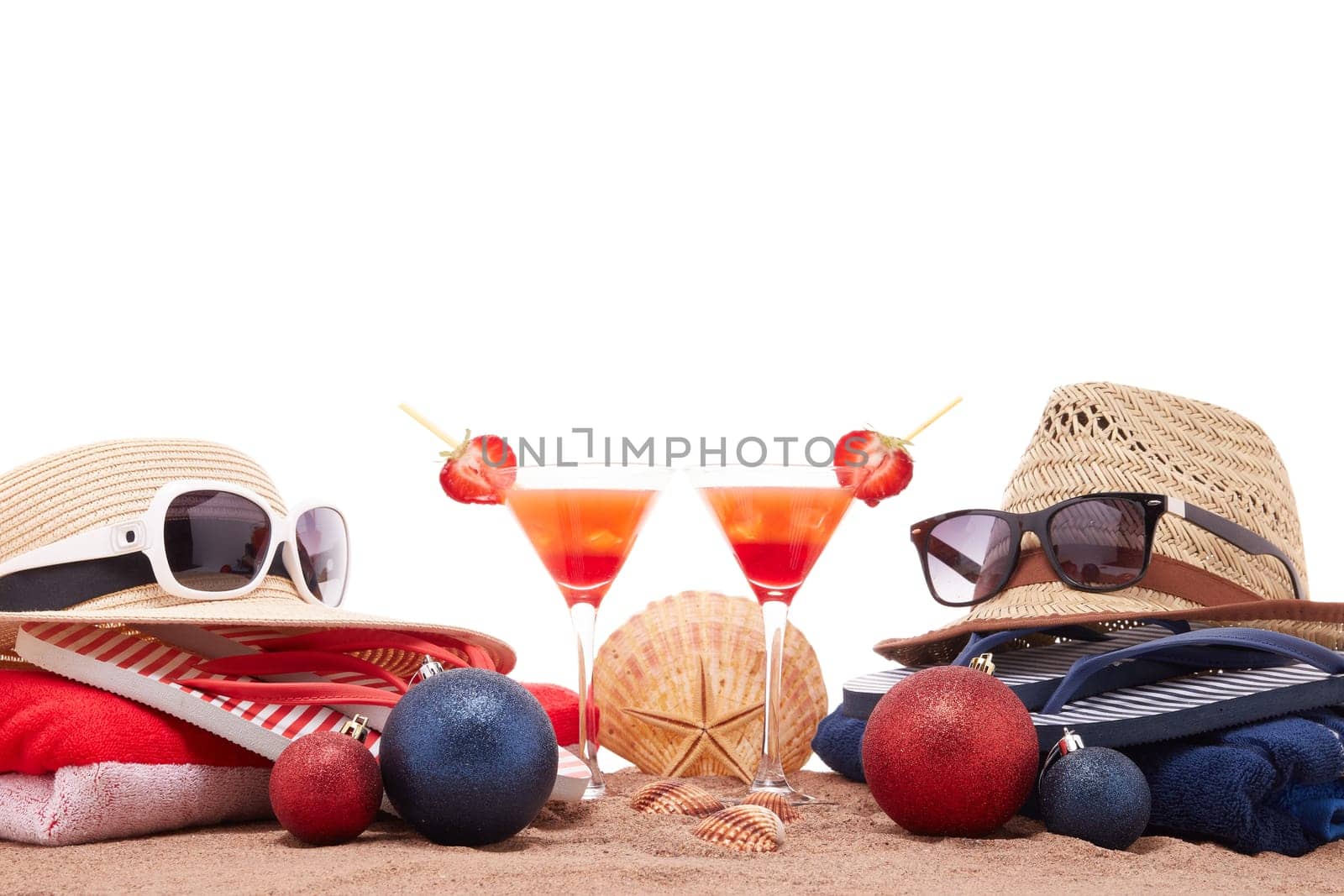 Beach accessories (flip flops, straw hats, seashells, sand, sunglasses), two glasses of cocktail, christmas ornaments on white background. Christmas. Winter vacation in warm countries, beach holiday