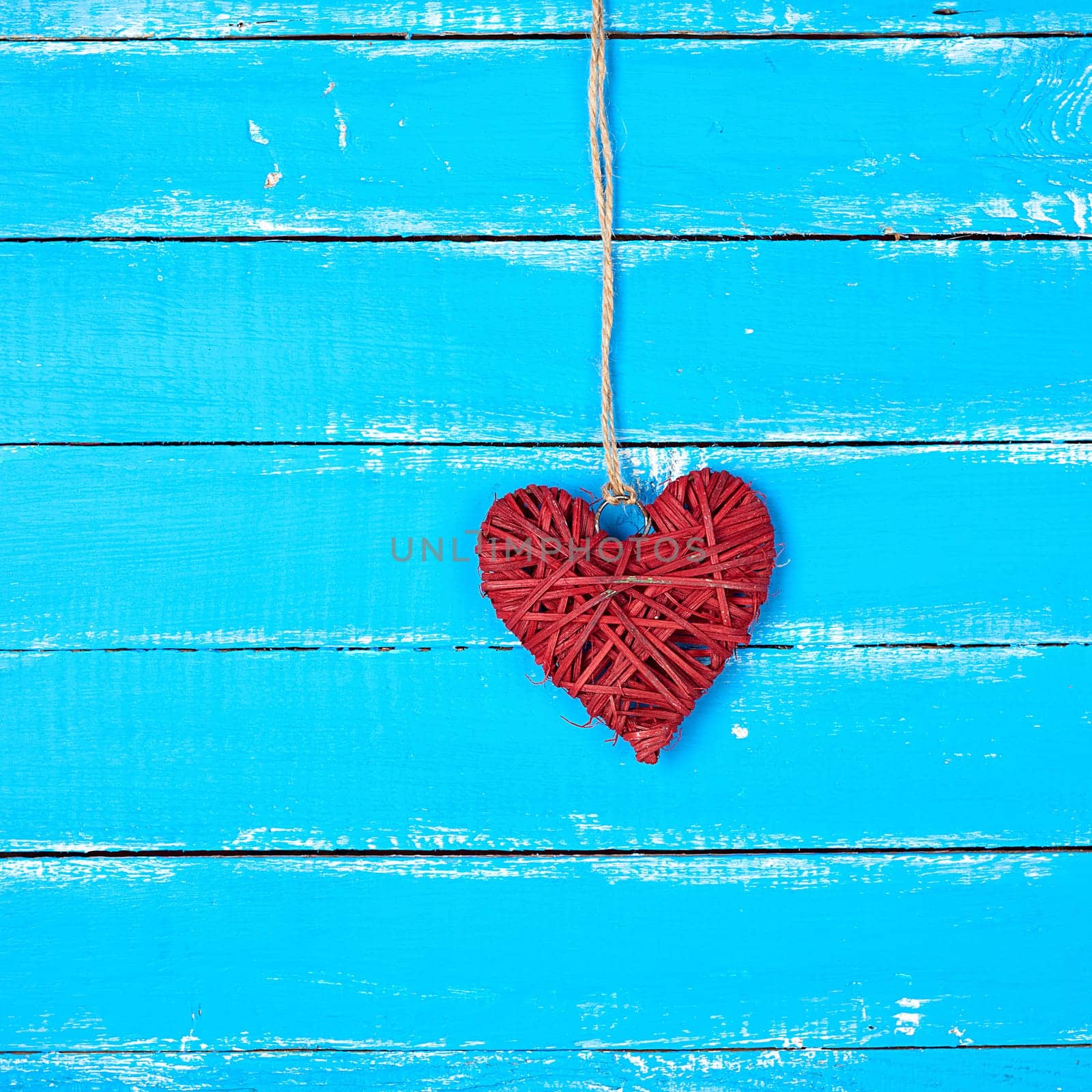 red  wicker decorative heart  hanging on a rope, blue wooden background, festive backdrop