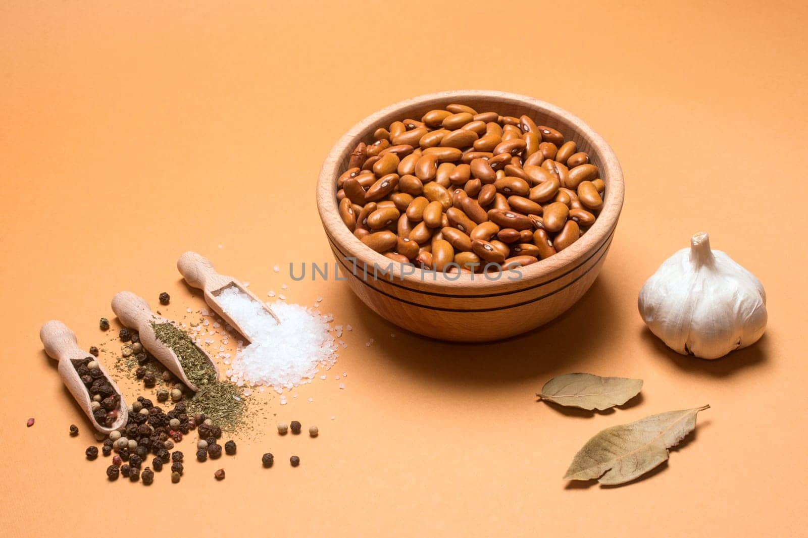 Brown bean seeds in wooden bowl with some herbs and spices on beige background.