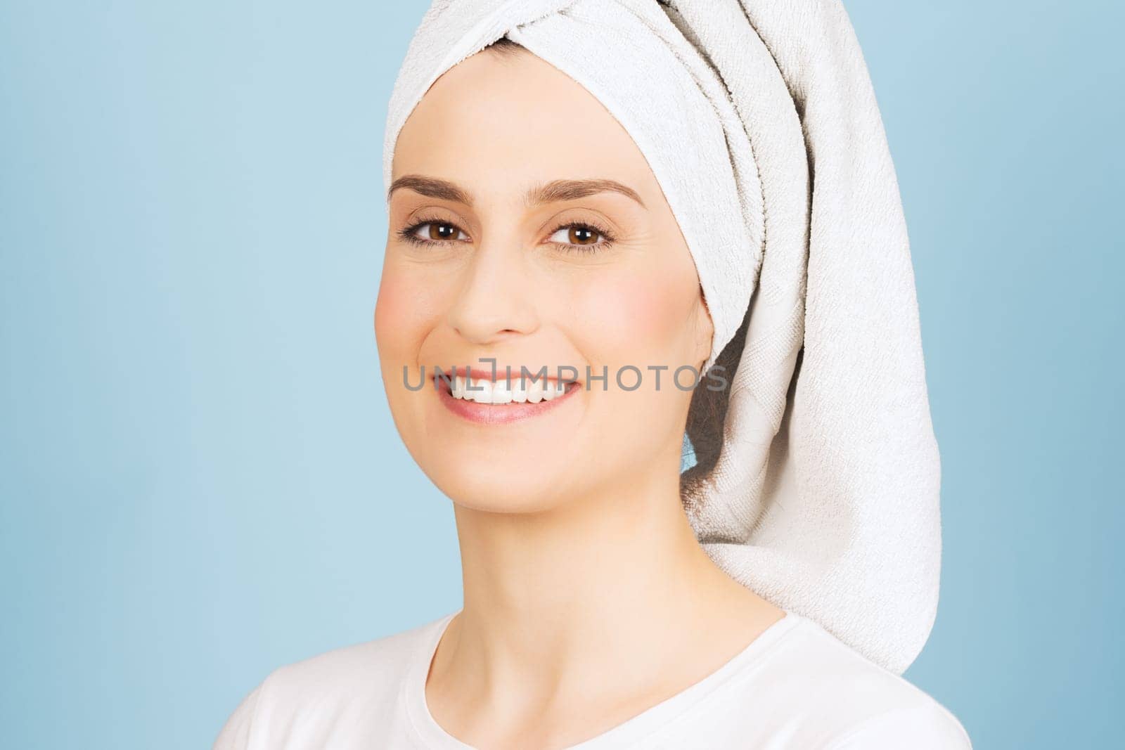 Beautiful smiling woman with white towel on head has natural make-up on blue background, natural beauty.