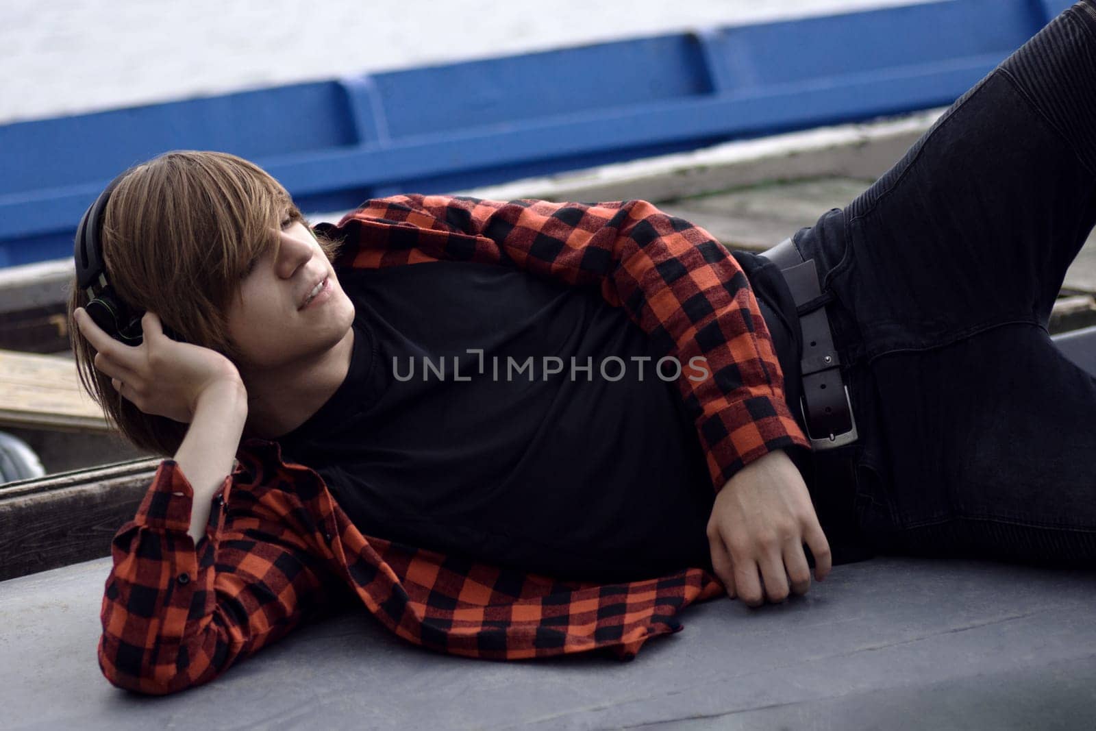 Trendy young guy in plaid shirt with headphones is listening music and enjoying outdoors.