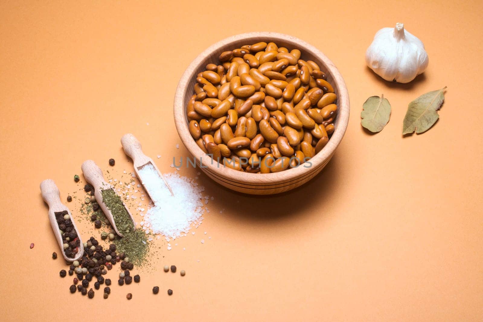Brown bean in wooden bowl with some spices and ingredients is on beige background.