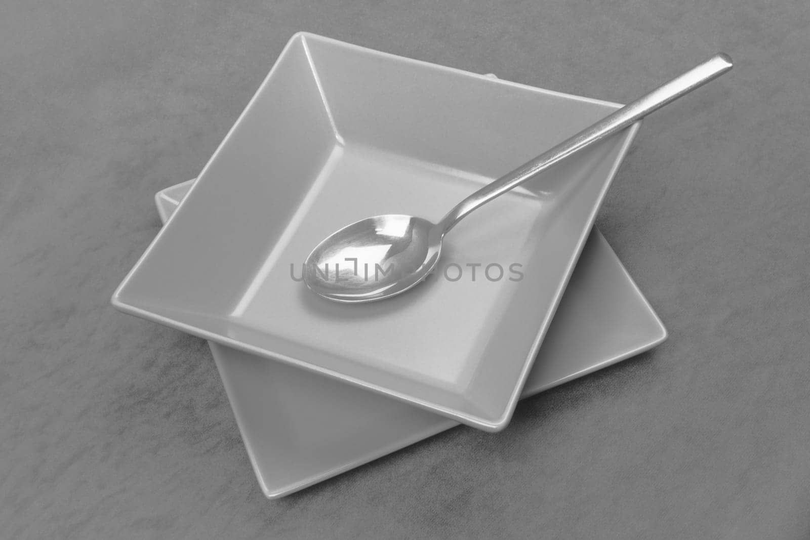 The gray square shaped plate with spoon is served on gray table, modern design crockery.