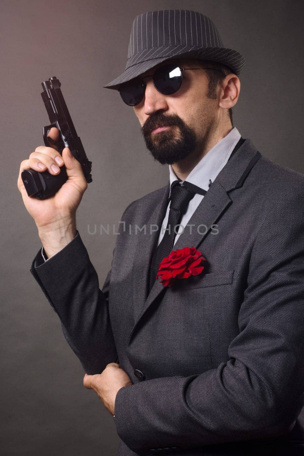 The old-fashioned elegant man in suit, hat and sunglasses is holding a pistol in hand.
