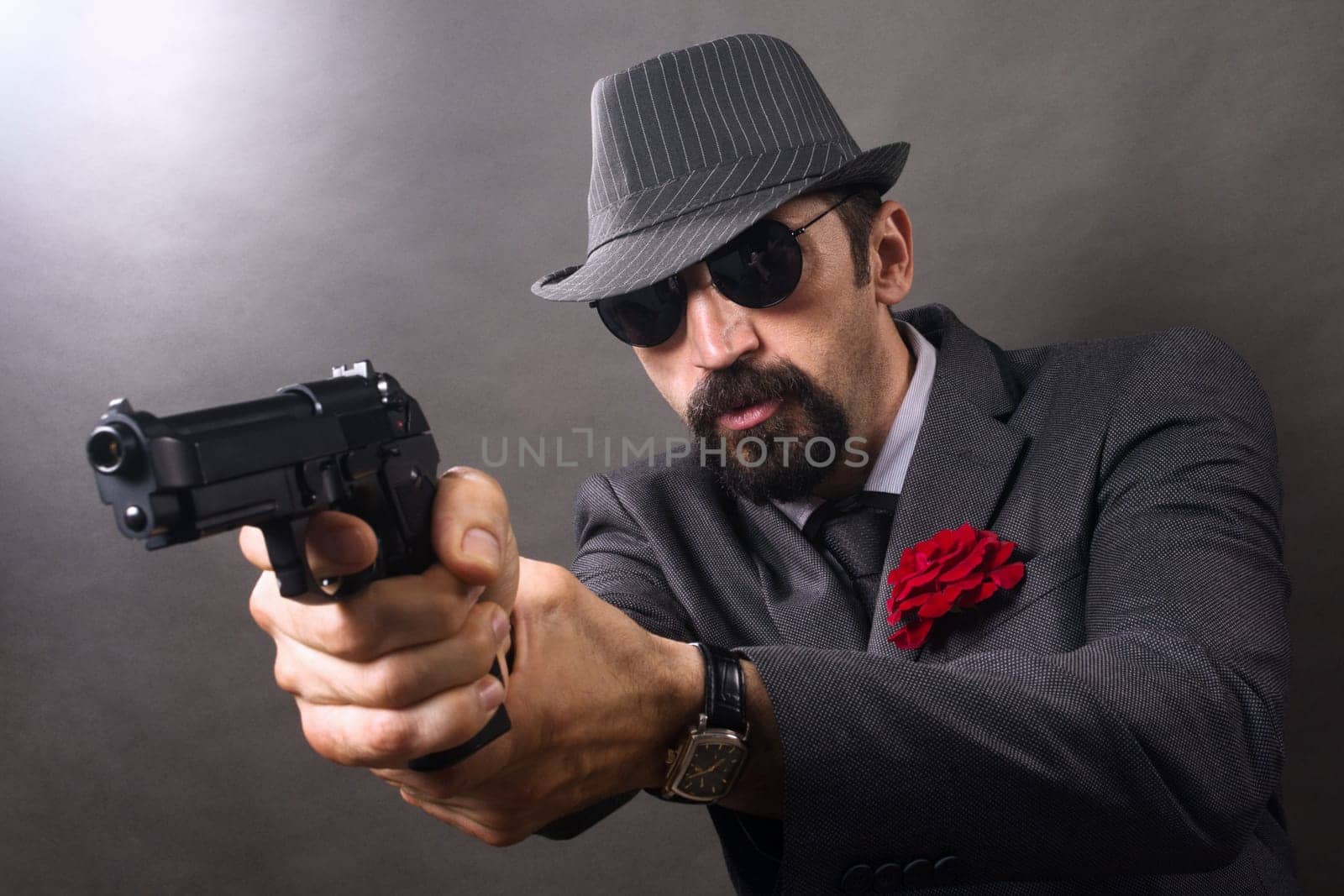 The gangster in elegant suit and hat in vintage style is aiming with pistol.