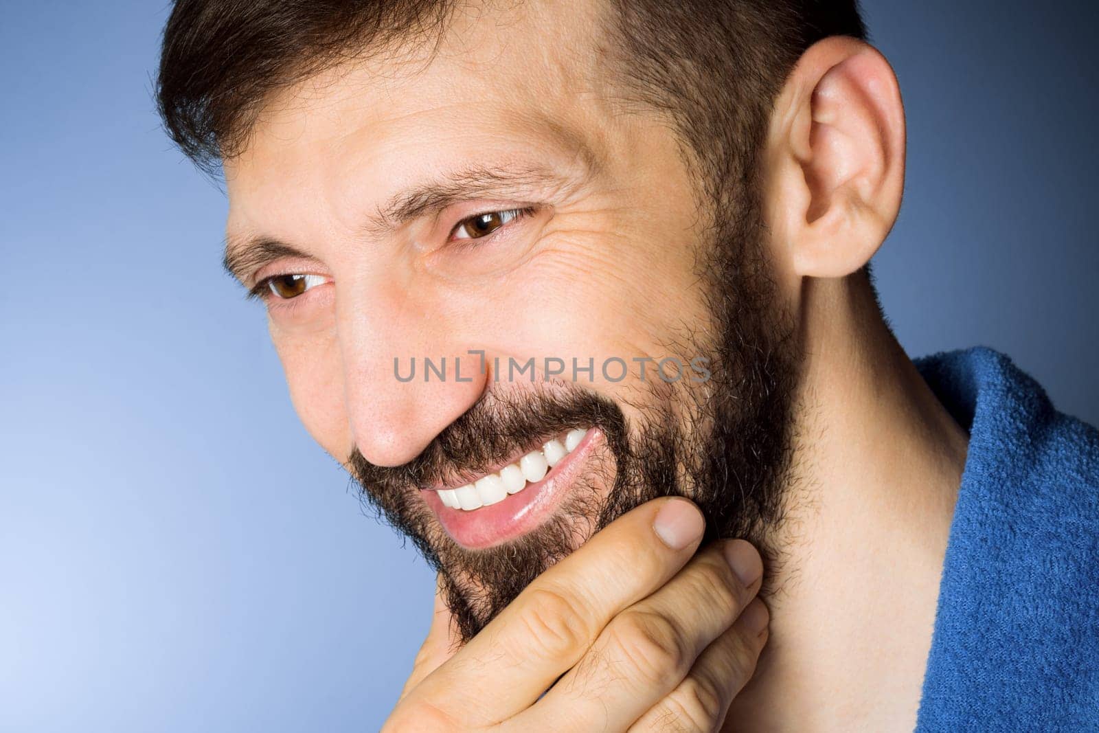 Close-up portrait of smiling middle aged bearded man on blue background.