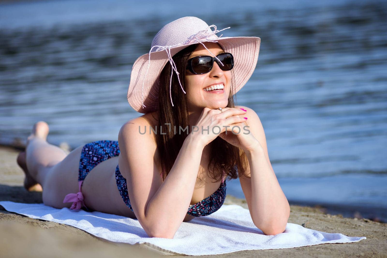 Attractive smiling woman in hat, sunglasses and bikini is enjoying in summer at the beach.