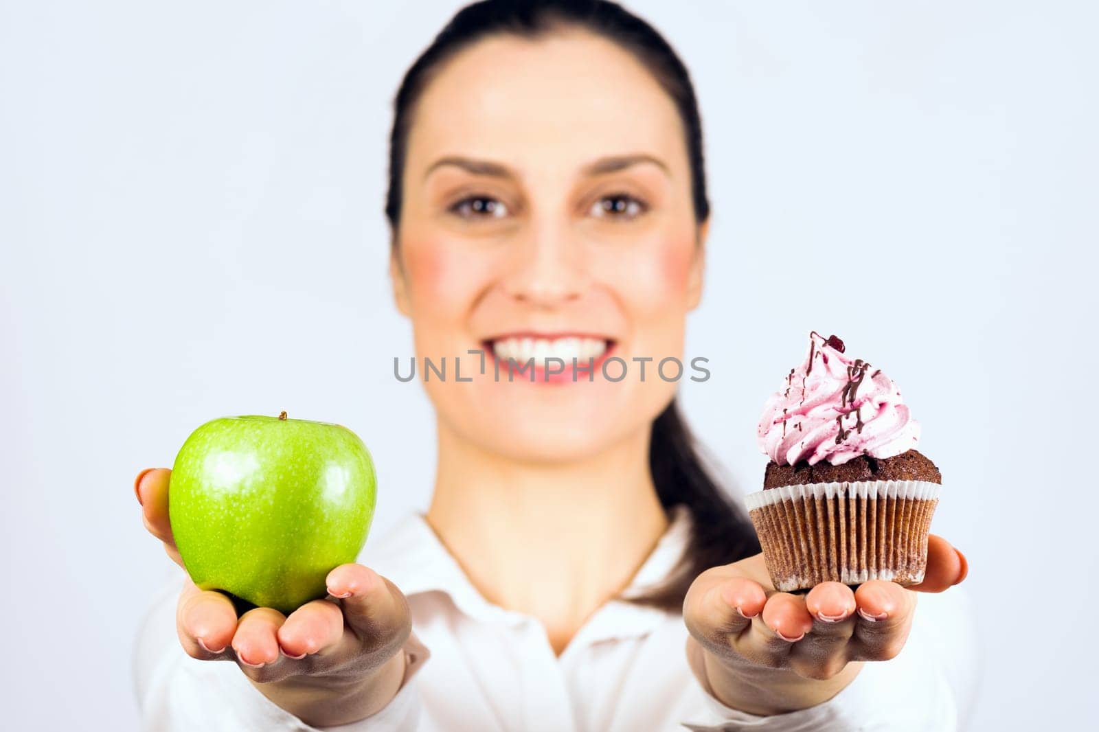 The smiling woman gives a choice to deciding apple or cupcake, healthy or unhealthy eating.