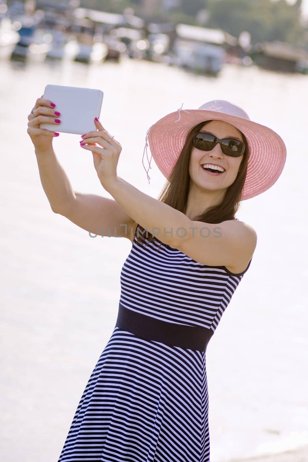 Attractive smiling woman tourist in hat is using digital tablet for photographing and enjoying in summer.