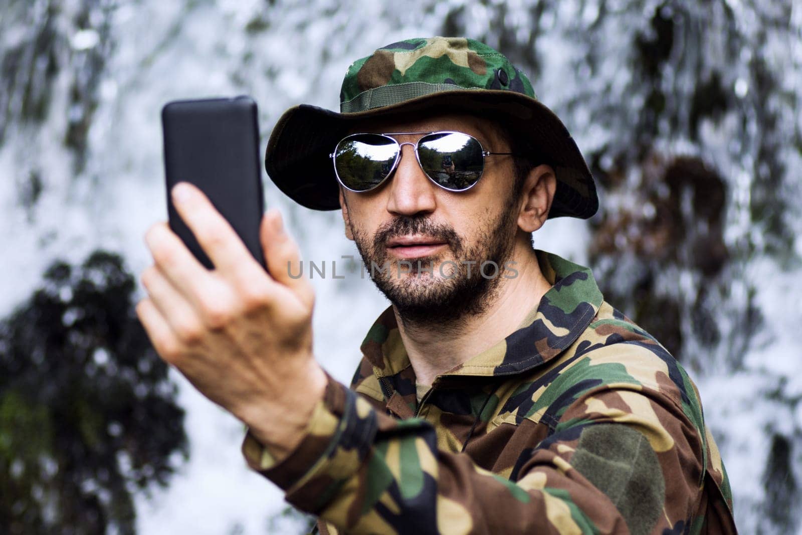 Man in military uniform is taking selfie and using phone in nature, adventure in nature.