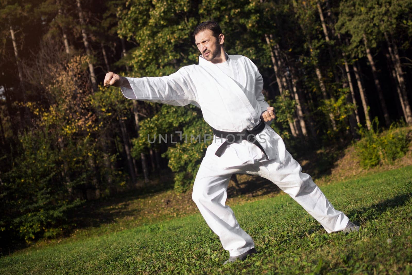 The middle aged man in white kimono and black belt is practicing martial arts in nature.