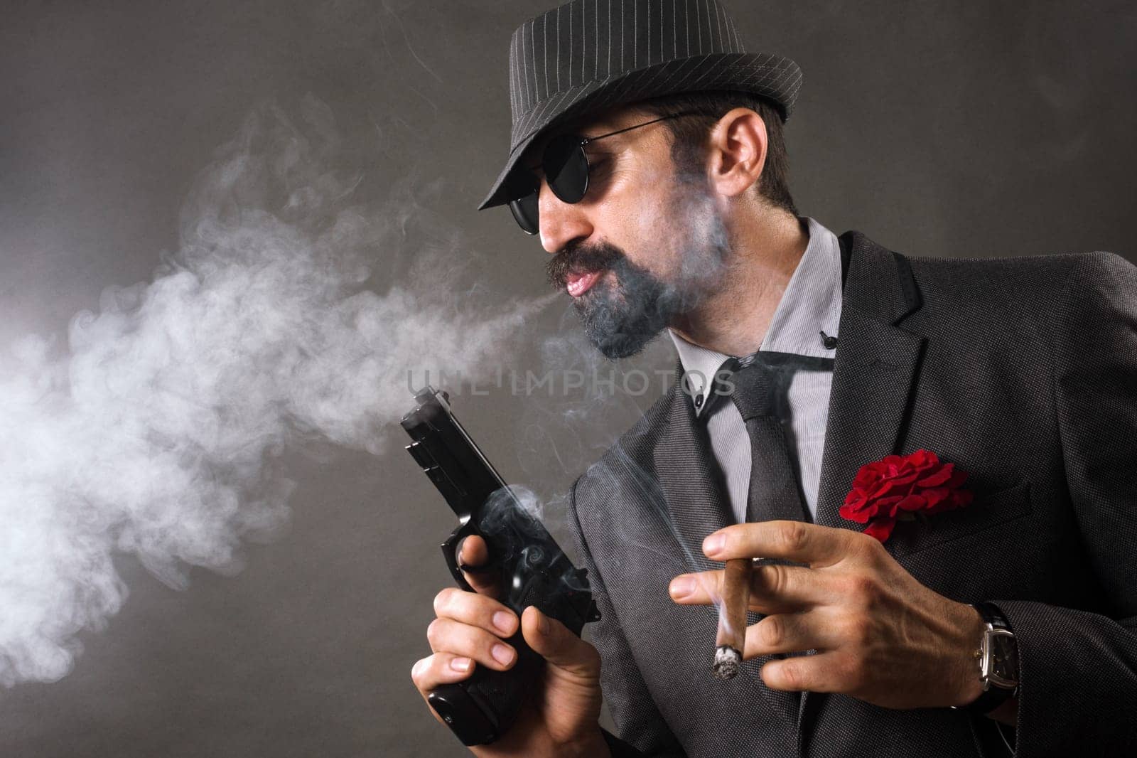 The elegant mafia boss or gangster is smoking cigar and holding pistol in hand.