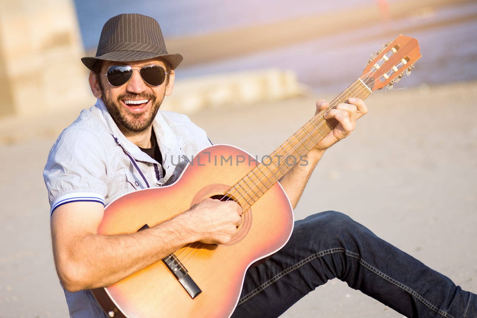The cheerful smiling guy is playing guitar and singing outdoors.