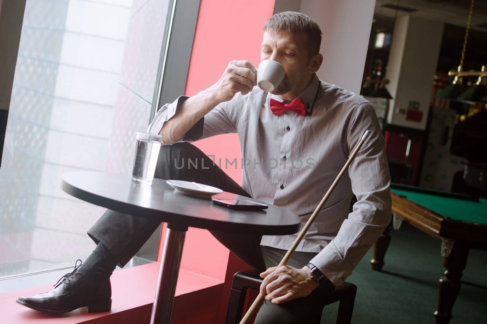 The billiard player is drinking coffee in billiard club.