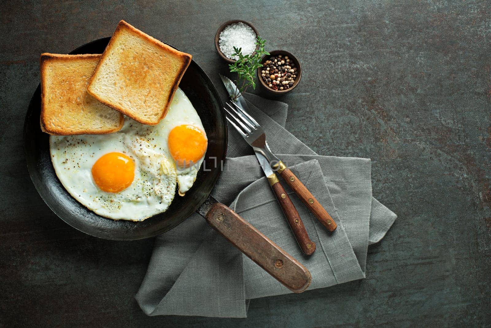 Pan of fried eggs with bread on dark table top view. Heathy breakfast food.