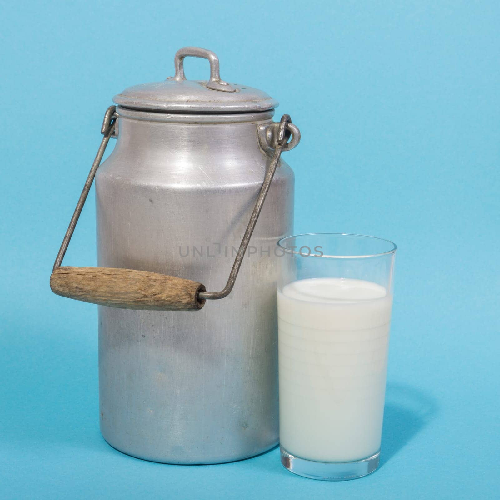 Glass of fresh milk and retro milk canister on blue background