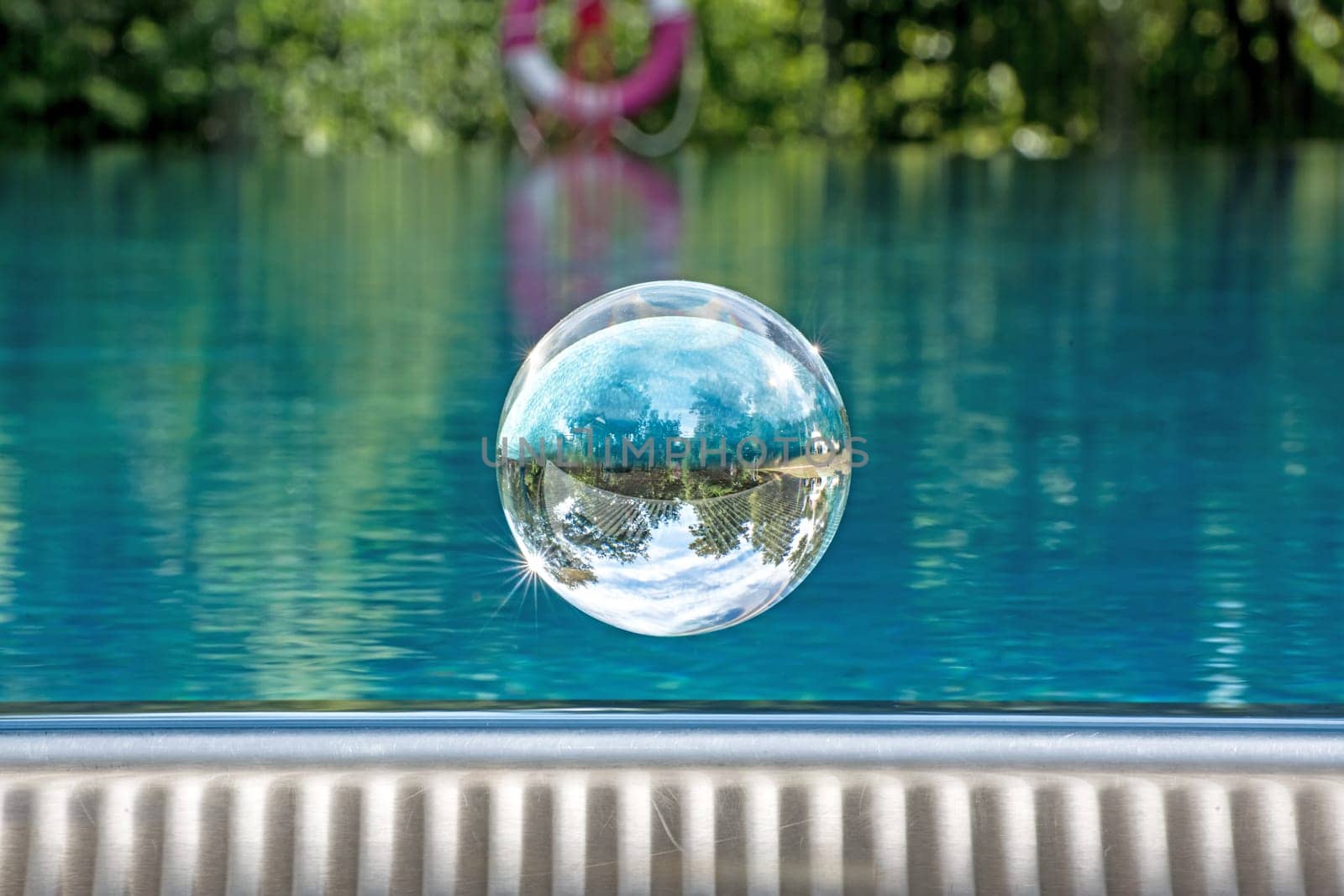 Glass ball hovers over a swimming pool with mirrored cloudy sky and trees