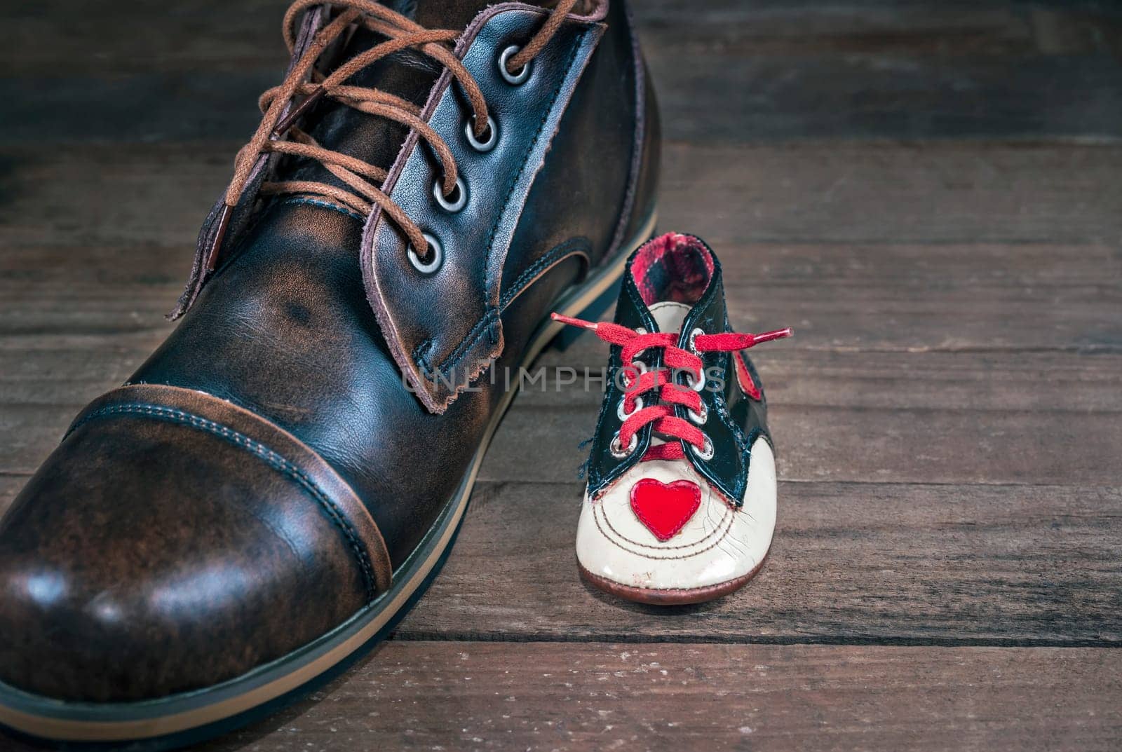 Newborn's shoe next to the same person's adult shoe. Concept image of growth, aging and evolution of fashion and design.