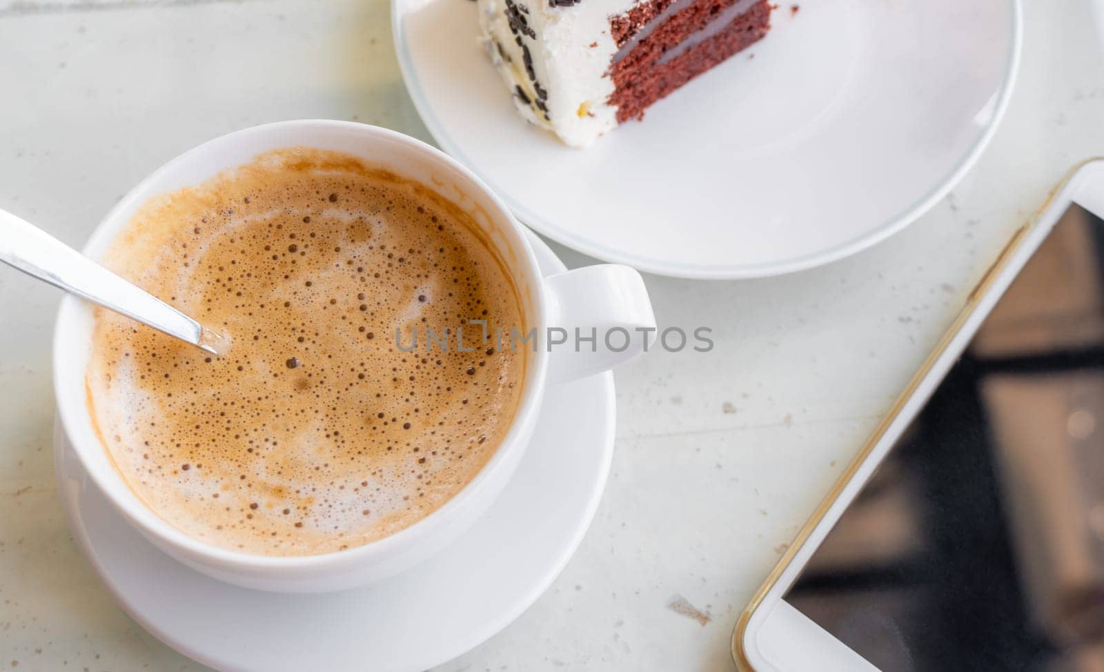 Latte coffee with smart phone in a white cup on white table blurred background