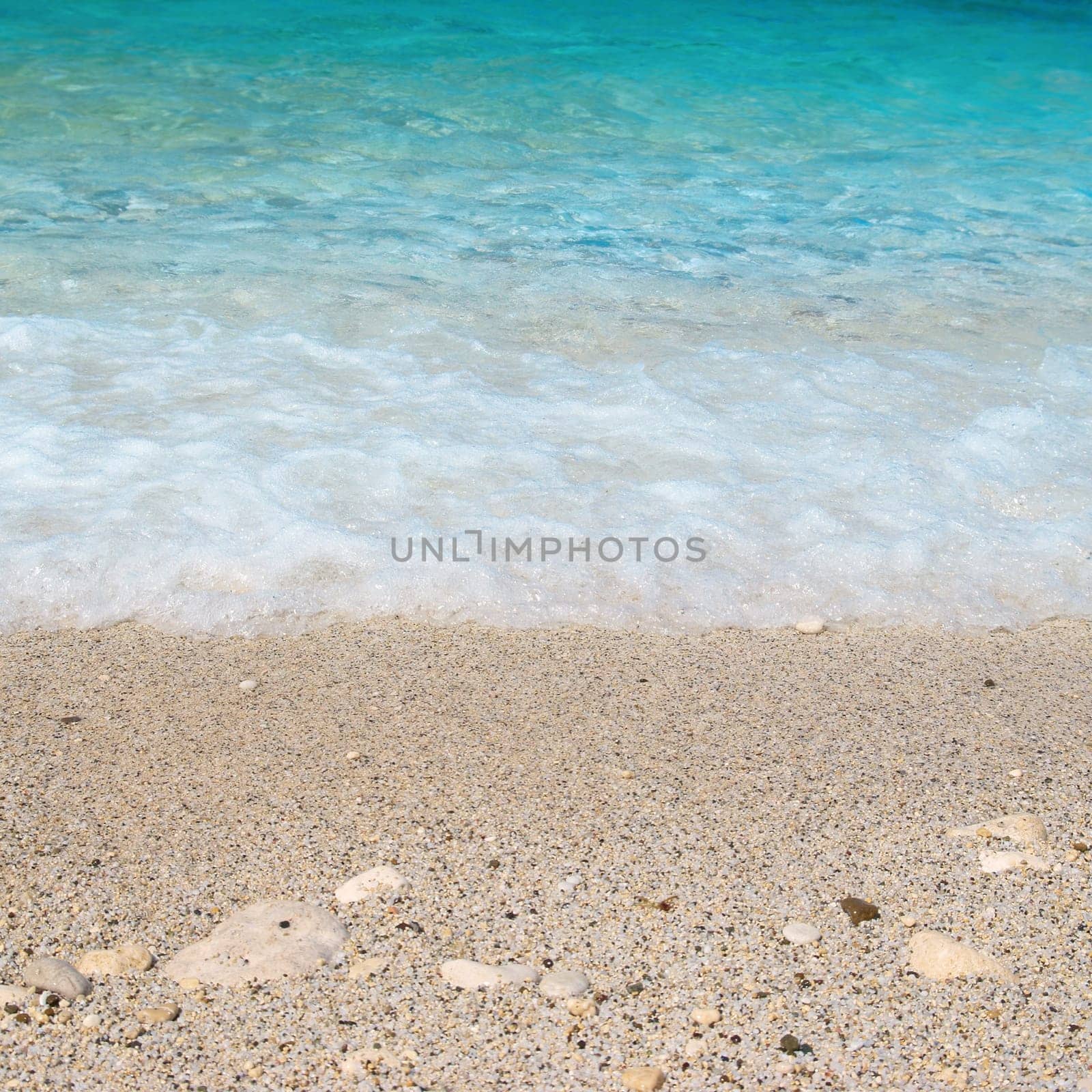 Tropical sand beach with sea waves and stones.
