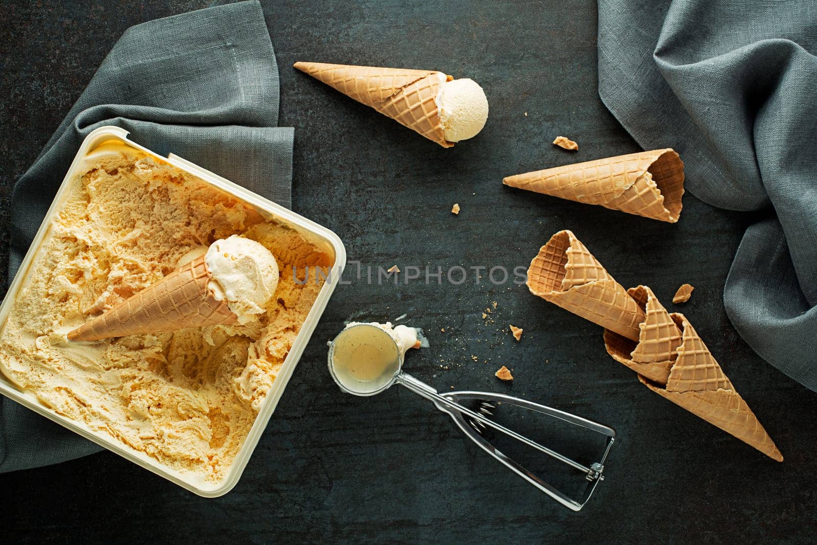 Vanilla ice cream scoops, scooped from container in to waffle cones with a silver utensil