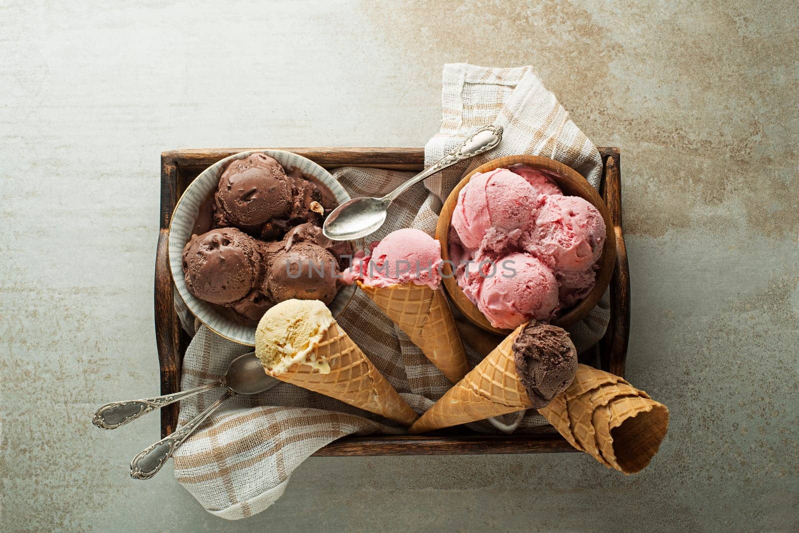 Ice cream scoops with chocolate, strawberry and vanilla flavors, scooped in to waffle cones and bowls