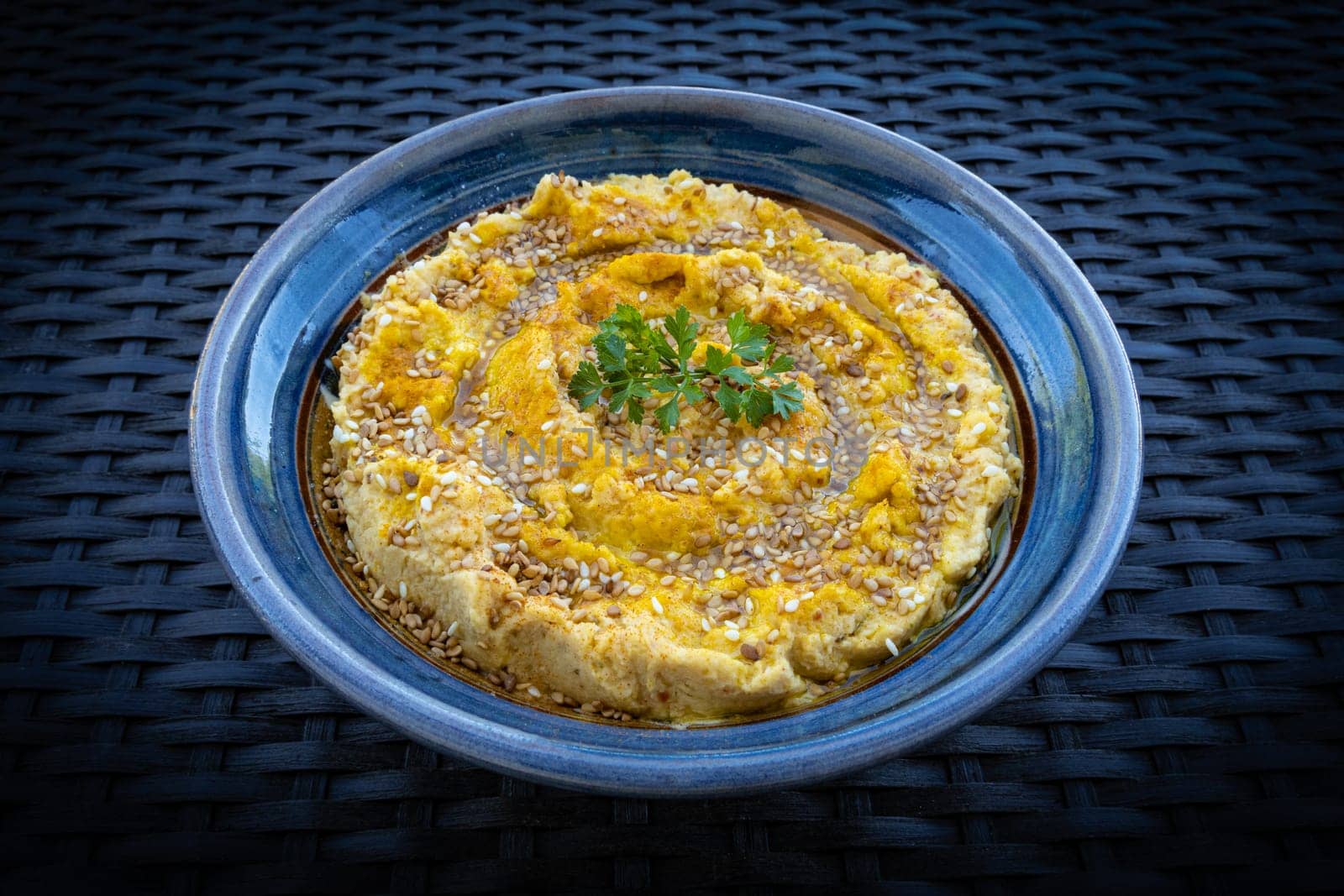 Tasty hummus (or houmous) in blue bowl on dark background