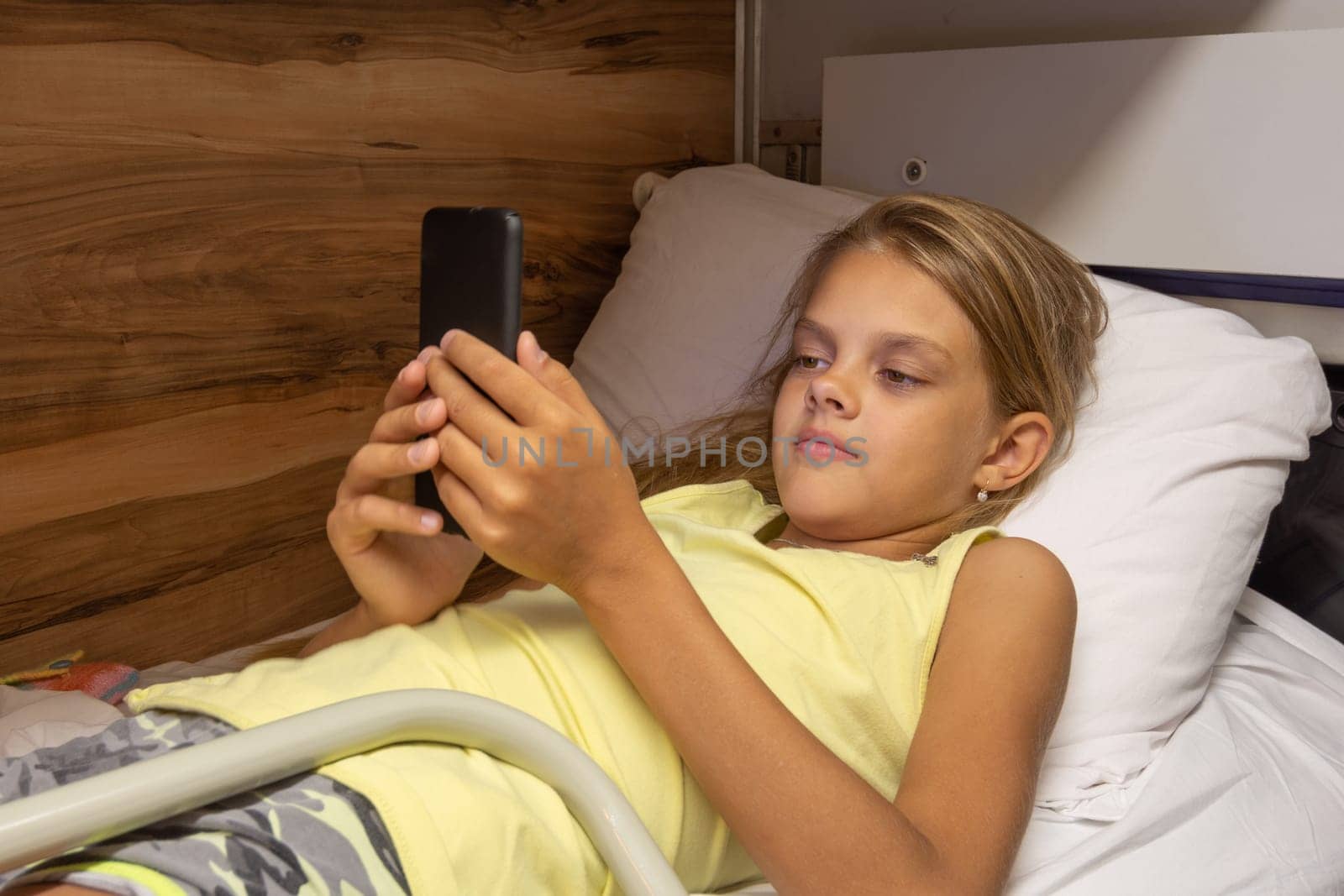 The girl lies on the top shelf in the carriage and plays in the smartphone