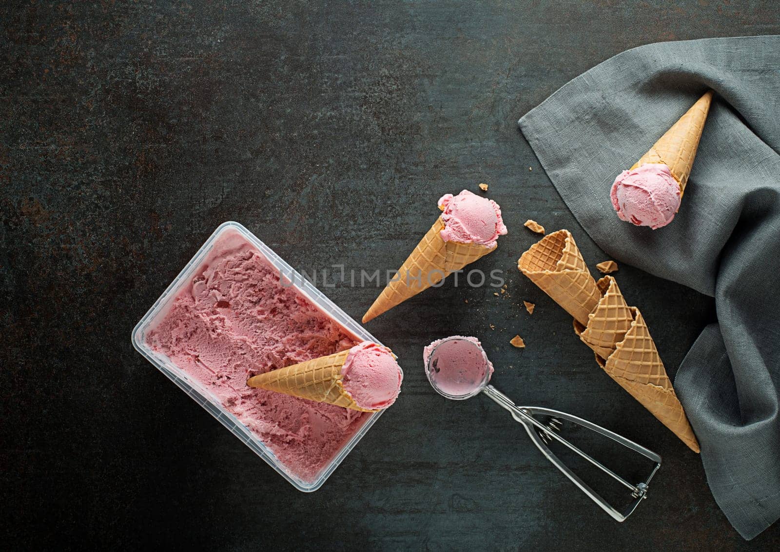 Fresh of soft ice cream or frozen yogurt with berry fruit flavours. Fruit ice cream scoops, scooped out of container in to waffle cones with a silver utensil