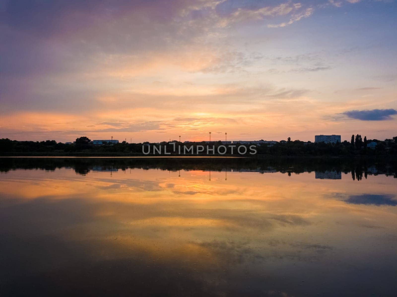Colorful sunset clouds symmetric reflected on the lake surface. Idyllic summer evening, natural scene near a countryside pond with calm water.