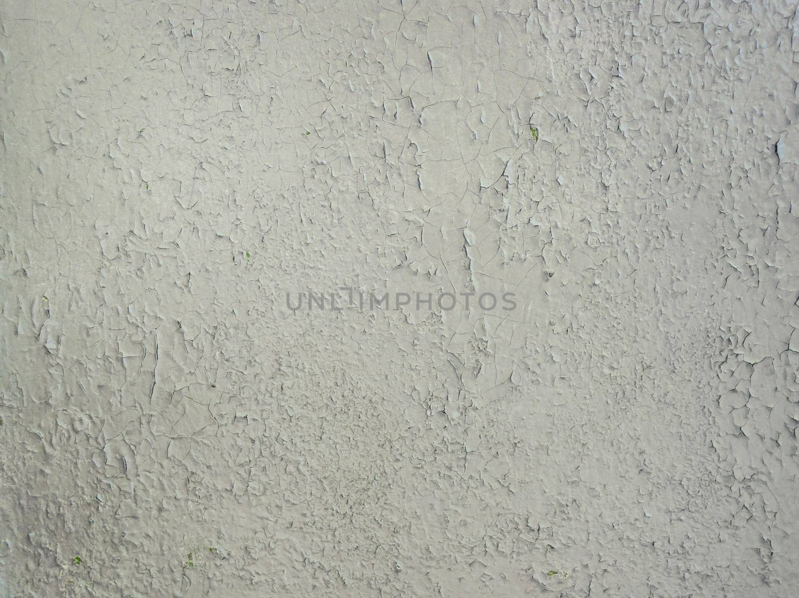 Grey paint peeling on a metallic surface background. Old grungy, weathered painted wall texture. Cracked, dirty, silver plaster falling off the construction structure.