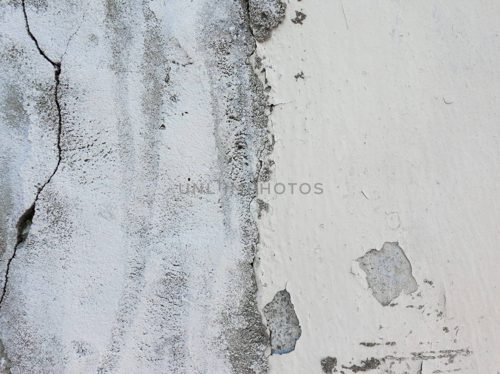 Old grungy, weathered concrete wall and cracked white paint peeling off the beton structure. Abstract construction element surface, dirty texture with plaster falling.