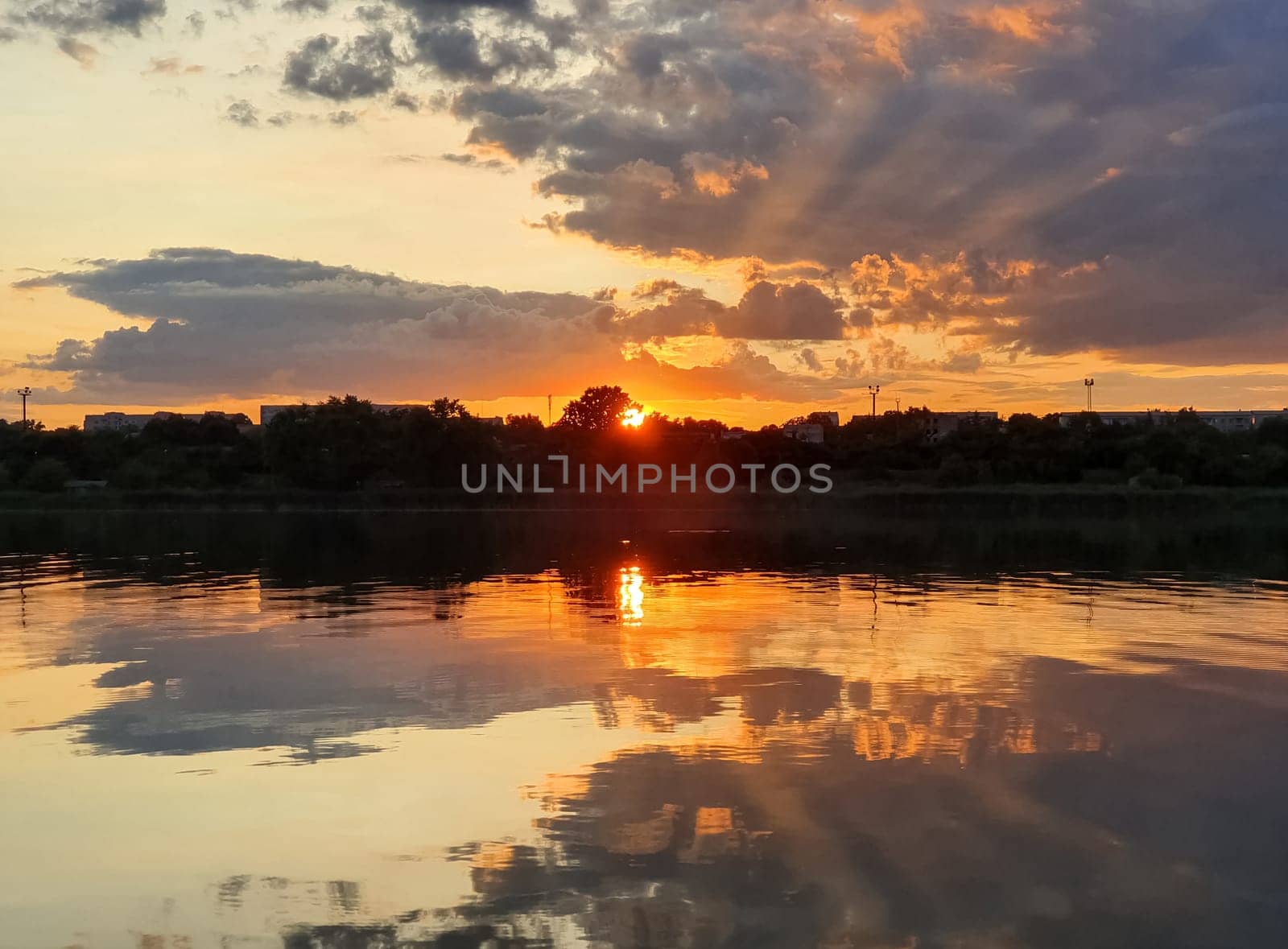 Wonderful sunset over the city horizon with reflection on the calm lake water in a silent summer evening..