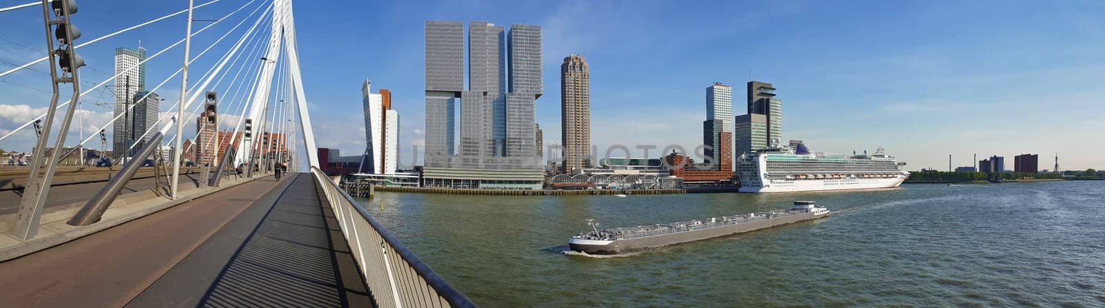 Cityscape panorama from Erasmus bridge over Meuse river in Rotterdam, the Netherlands. Tall modern buildings on the horizon and big ships crossing the Erasmusbrug canal.