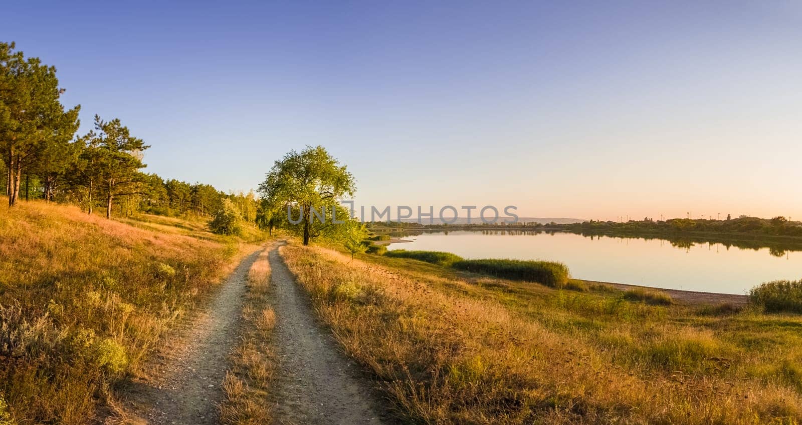 Scenic countryside landscape with rural dirt road across a meadow with dry grass and hay under a clear blue sky. Autumn panorama view near Delia lake, Ungheni, Moldova.